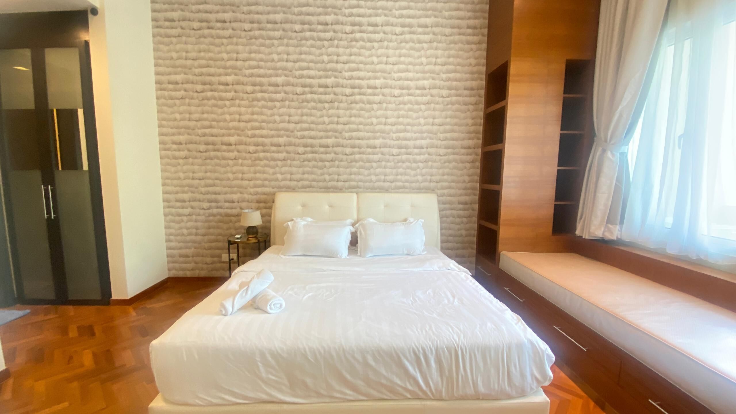 Una habitación de hotel con una cama grande, una mesita de noche, una lámpara y una ventana con cortinas.