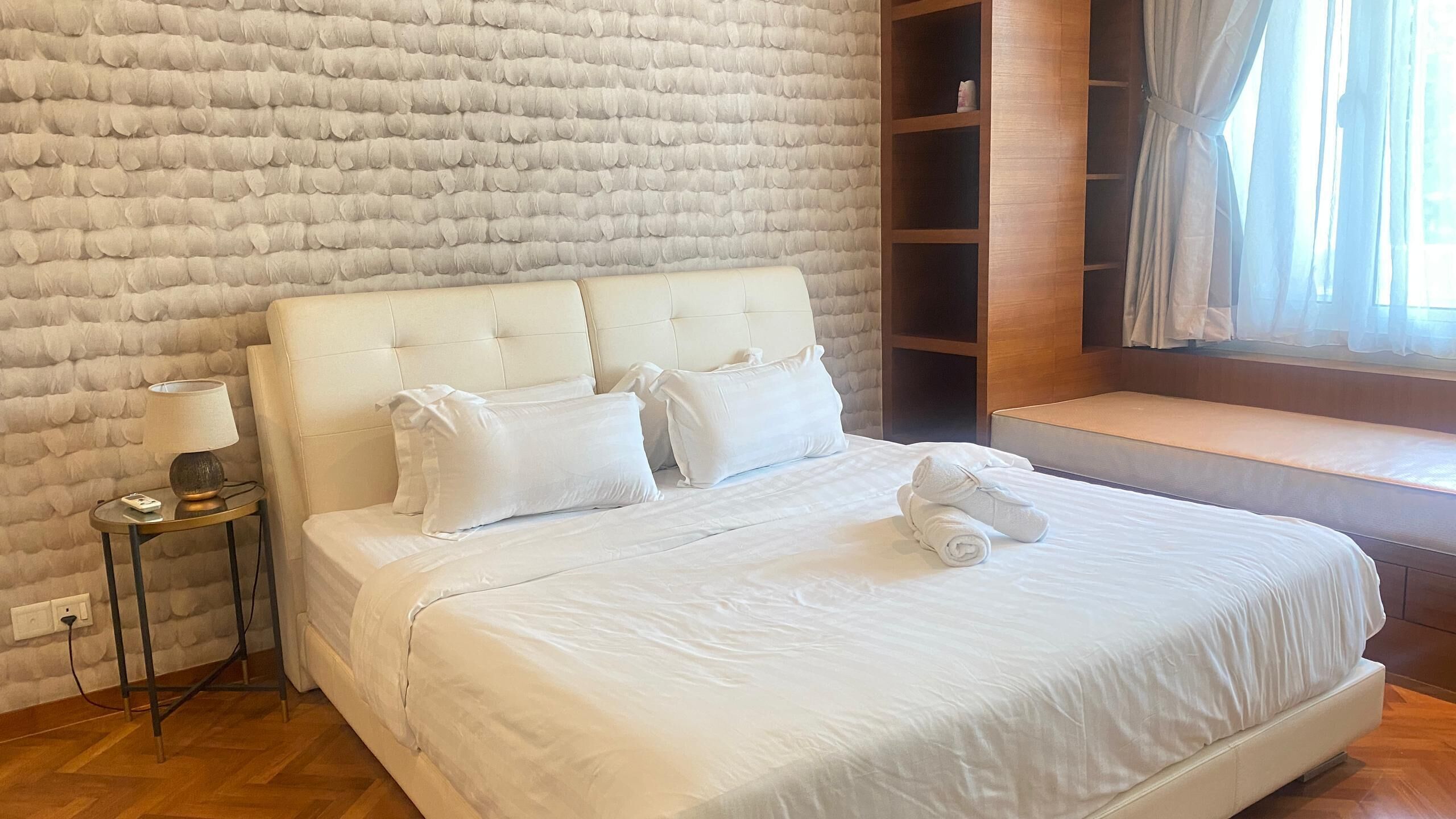 Ein ordentlich gemachtes Bett mit weißen Leinen, einer Nachttischlampe und einem Holznachttisch.