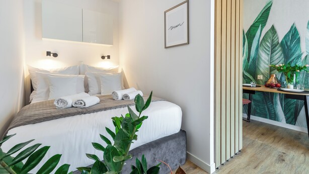 Una habitación de hotel moderna con una cama bien hecha, un ventanal grande y una obra de arte colgada en la pared.