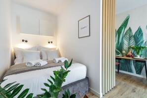 A modern hotel room with a neatly made bed, a large window, and a wall-mounted artwork.