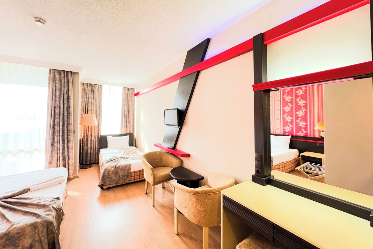 A hotel room with a bed, a desk, a chair, a TV, and a large mirror.