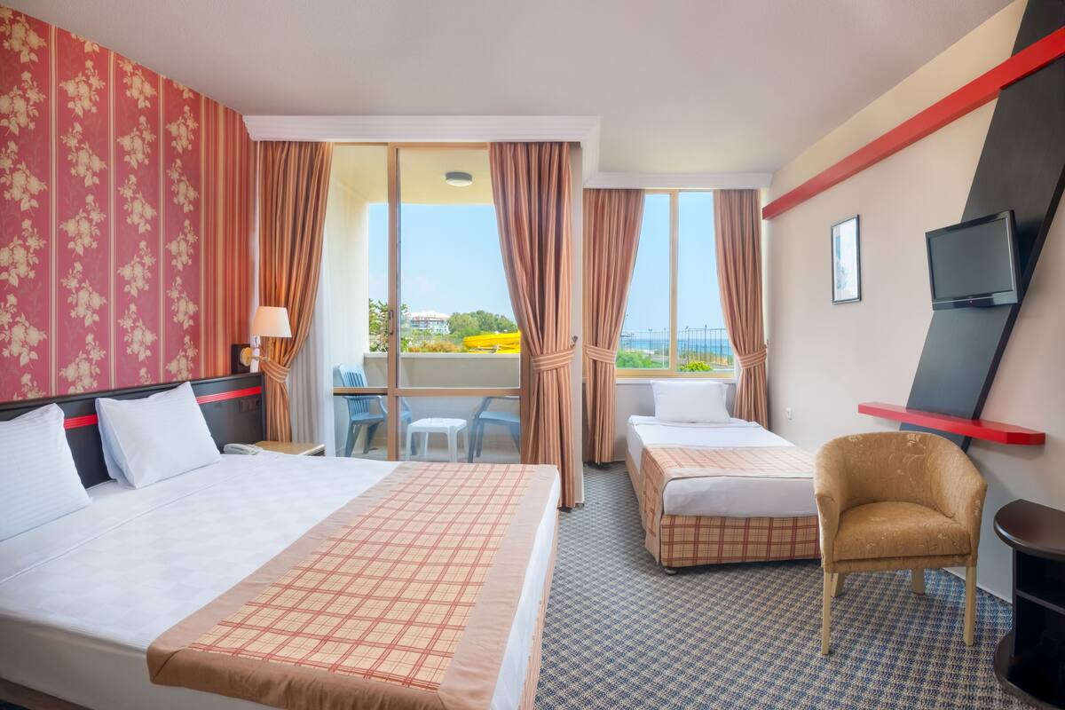 A hotel room with two beds, a TV, a chair, and a balcony with a view.