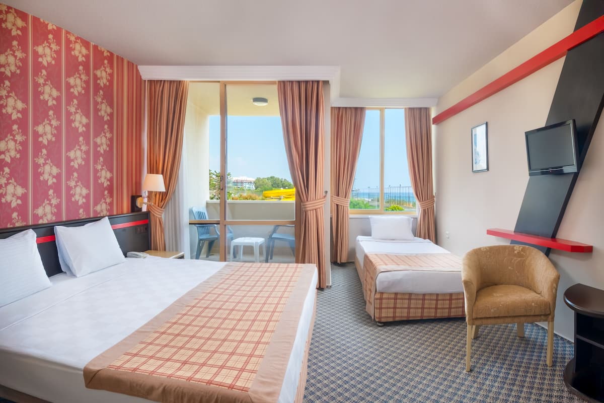 Ein Hotelzimmer mit zwei Betten, einem Fernseher, einem Sessel und einem Balkon mit Aussicht.