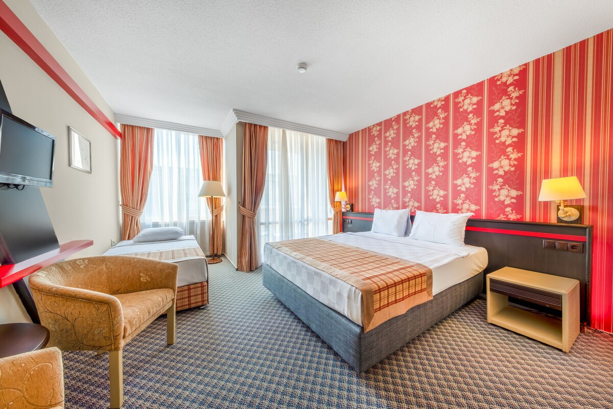 A hotel room with a bed, two chairs, a TV, a desk, and a nightstand with lamps.