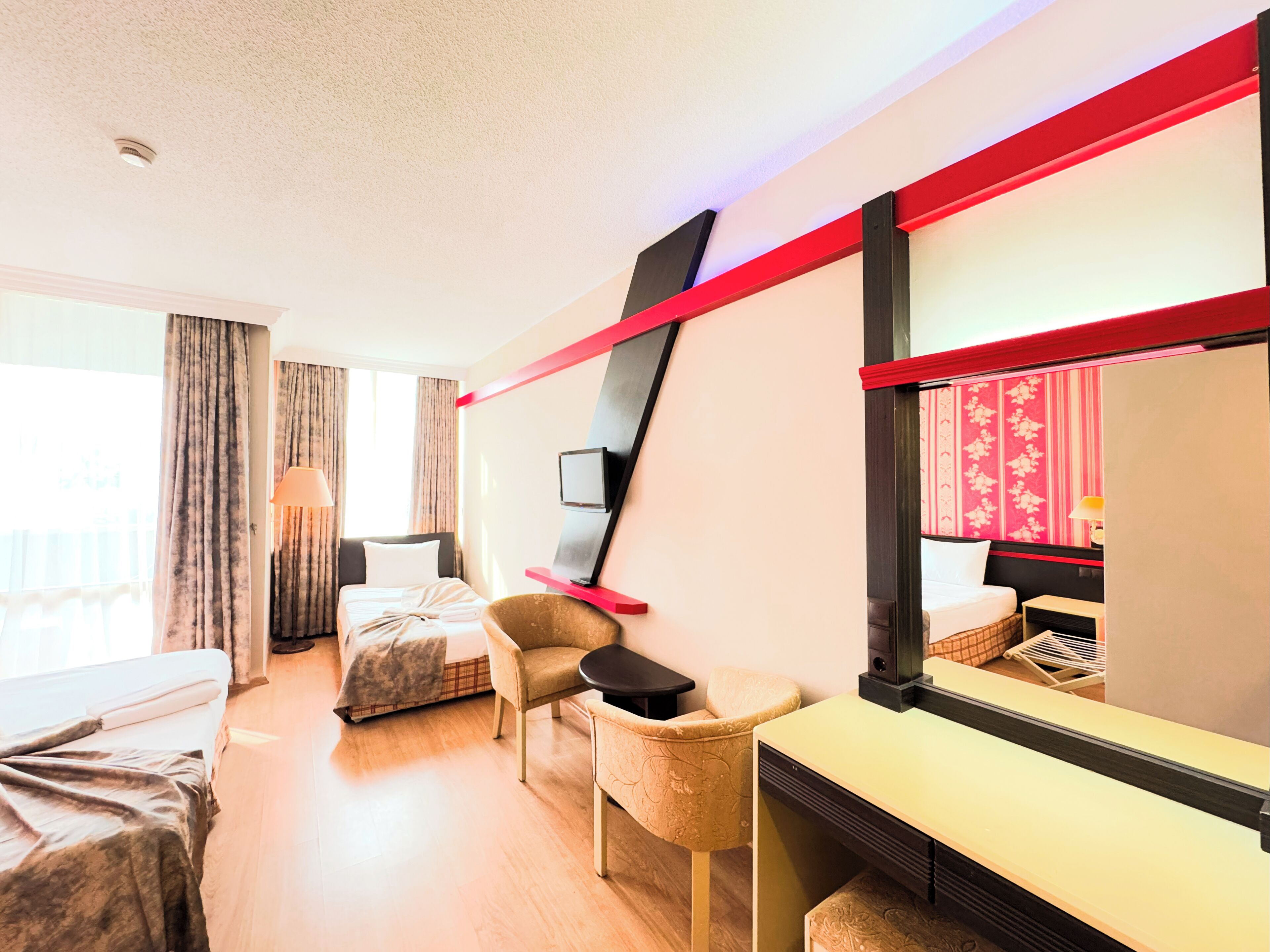 Ein Hotelzimmer mit Bett, Schreibtisch, Stuhl, Fernseher und einem großen Spiegel.