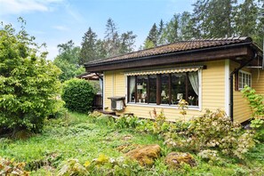 A yellow wooden house with a tiled roof, surrounded by lush greenery and trees. - Cozy holiday accommodation in Skebobruk, Norrtälje | SE13036 (Skebobruk)