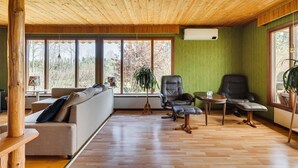 A room with a wooden ceiling, large windows, a sofa, two chairs, a small table, and a radiator.