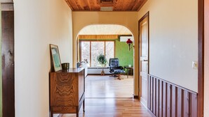 A hallway with wooden flooring, a wooden ceiling, and a green wall. There is a chair and a table with a lamp.