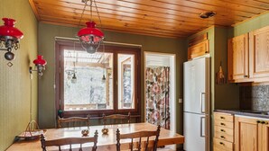 A wooden dining table with chairs, a refrigerator, wooden cabinets, and a window with a view of trees.