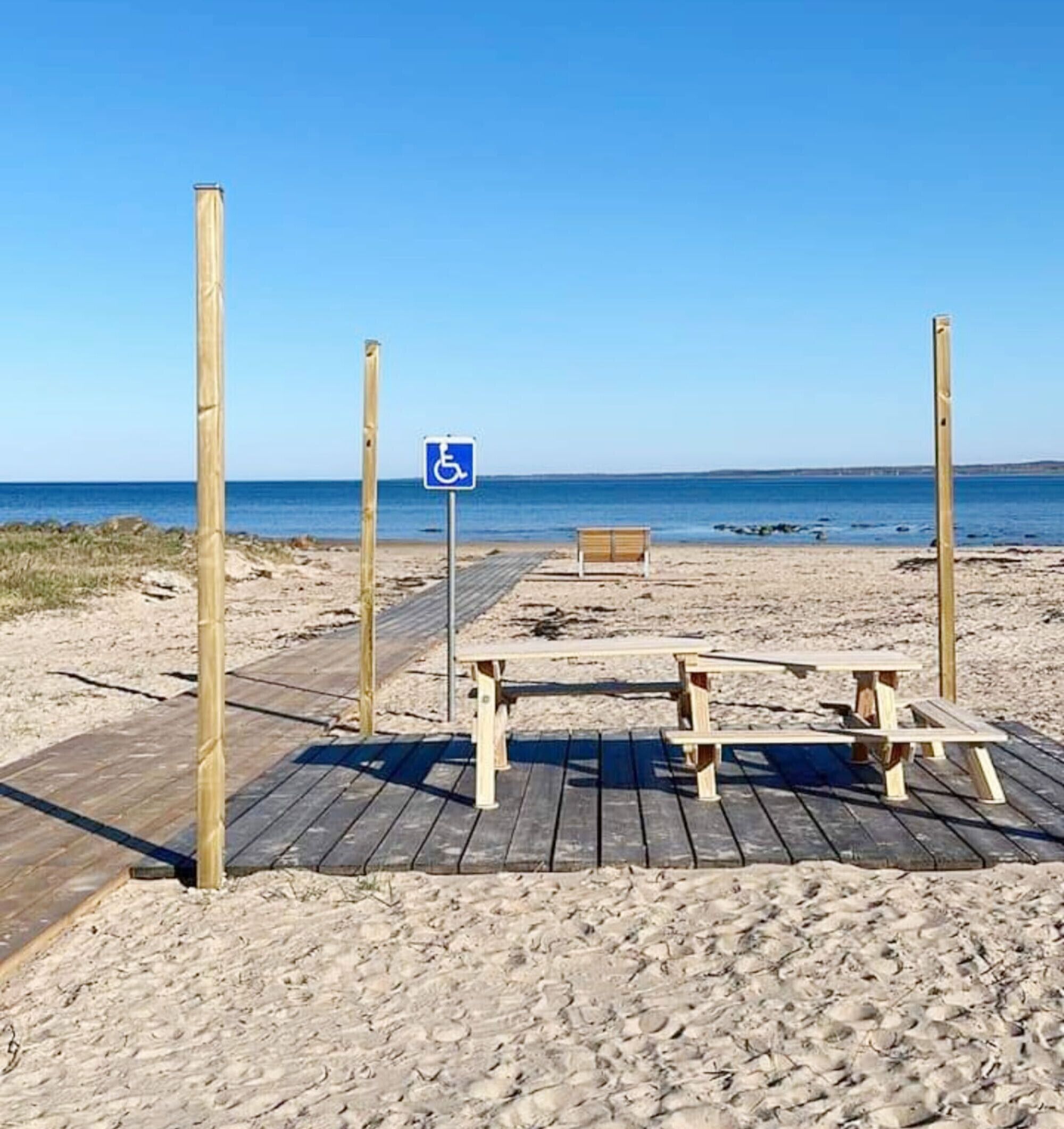 A beach with a wheelchair-accessible sign, wooden benches, and a wooden walkway leading to the beach.