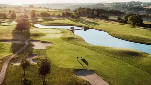 A golf course with a pond, trees, and a path.
