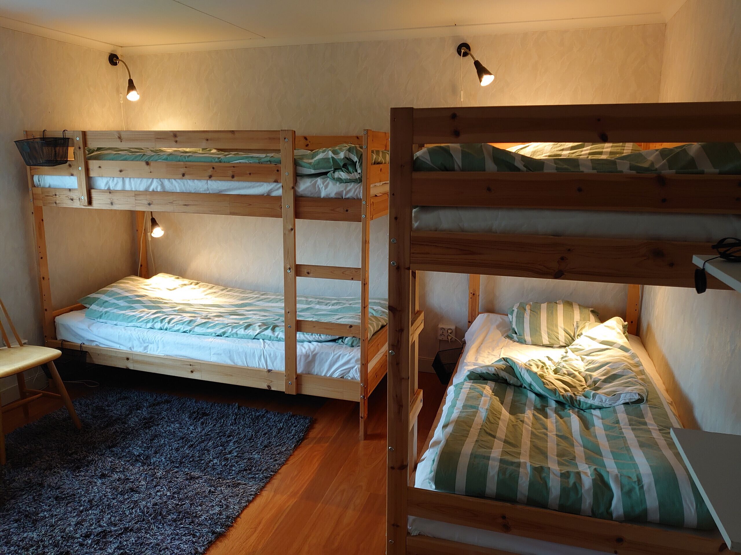 Une chambre avec un lit superposé, un bureau et une chaise, un petit tapis et une lampe fixée au mur.