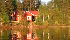 Punakatolla ja valkoisilla koristeilla varustettu mökki, jonka ympärillä on puita ja rauhallinen järvi.