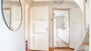 A hallway with white doors, a wooden floor, and a kitchen area visible through an open door.