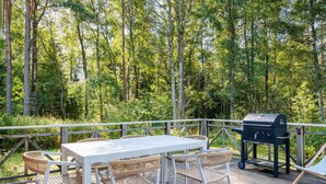 A deck with a table and chairs, a grill, and a wooden railing overlooking a forest.