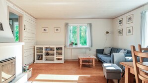 A cozy living room with a fireplace, a sofa, a wooden table, and a window with curtains.
