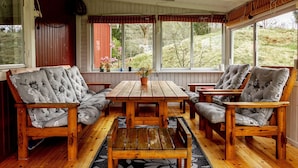 A cozy room with a wooden table and chairs, large windows, and a view of greenery outside.
