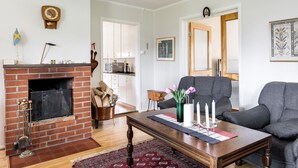 A living room with a fireplace, a sofa, a coffee table, and a kitchen in the background.