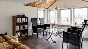 A cozy living room with a high ceiling, a bookshelf, a glass coffee table, and wicker chairs.