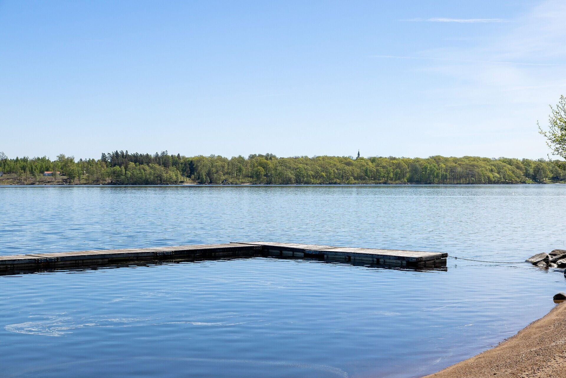 A calm lake with a wooden dock extending into the water, surrounded by a forested shoreline.