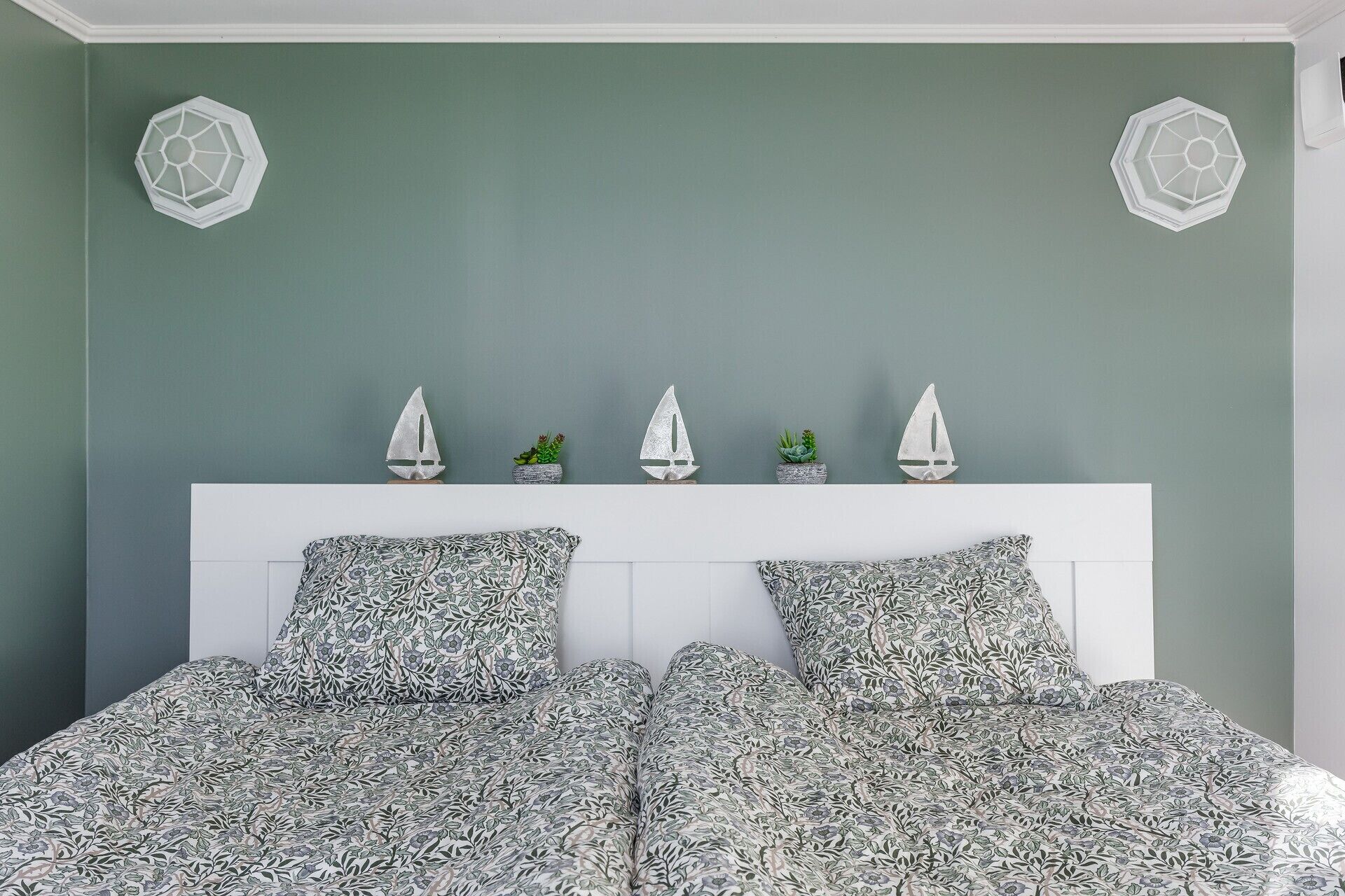 A bedroom with a green wall, a white headboard, and a floral-patterned bedspread.