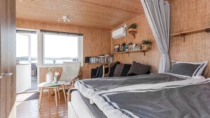 Een slaapkamer met een bed, een stoel, een klein tafeltje, een boekenkast en een raam met uitzicht.
