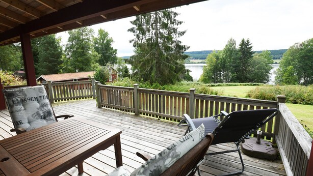 A wooden deck with a table and chairs, overlooking a lake and forested area.