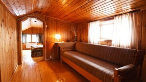 A wooden cabin interior with a sofa, a lamp, and a window with curtains.