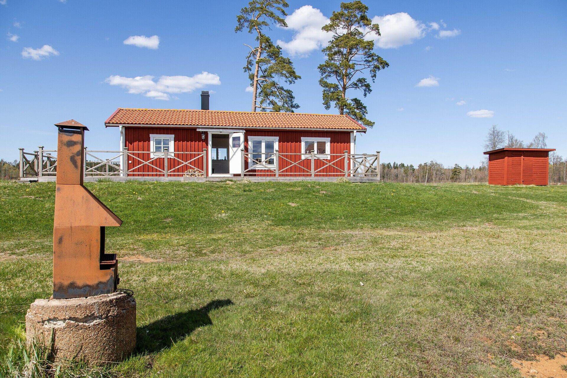 A red barn with a white door and windows, surrounded by a grassy field and trees.