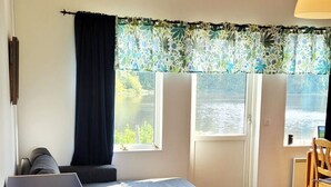 Een kamer met een bank, een klein rond tafeltje, een radiator en uitzicht op een waterpartij door een raam.
