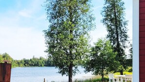 Een houten terras met uitzicht op een meer, omringd door bomen en een rood gebouw.