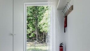 Ein Flur mit einer Tür, die zu einem bewaldeten Gebiet führt, einem an der Wand montierten Feuerlöscher und einem Kleiderständer mit Kleiderbügeln.