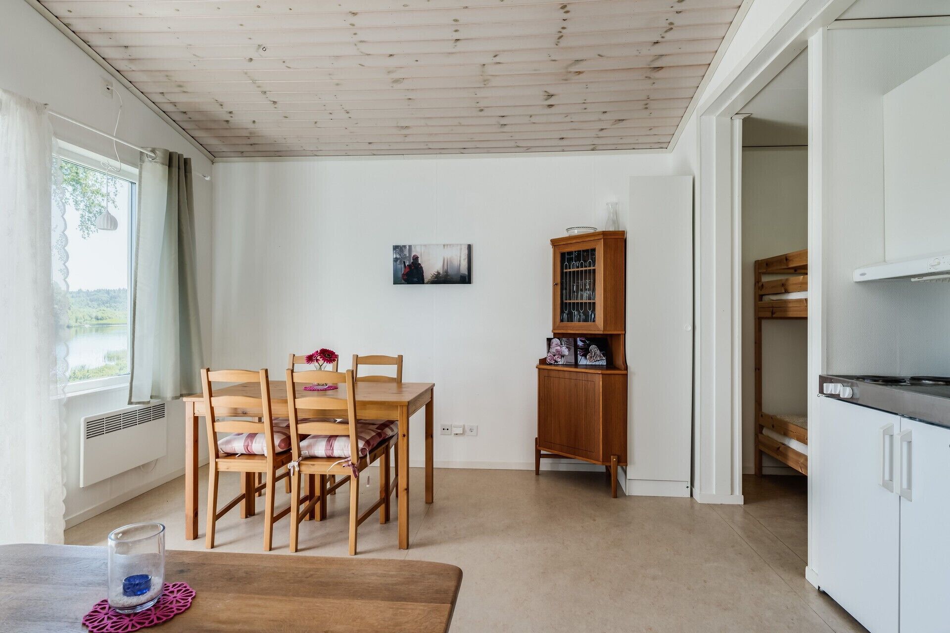 A dining area with a wooden table and chairs, a cabinet with glass doors, and a bunk bed in the adjacent room.