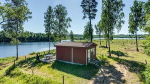 Eine kleine Holzhütte mit einem Ziegeldach, umgeben von einer Rasenfläche und Bäumen, in der Nähe eines Gewässers.