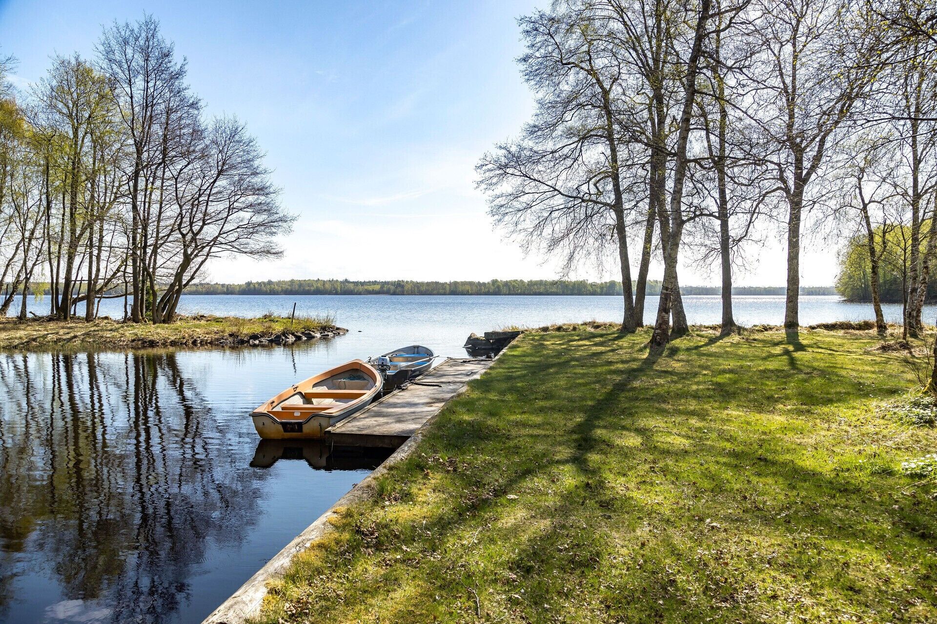 Un lago tranquilo con barcos amarrados a un muelle de madera, rodeado de árboles.