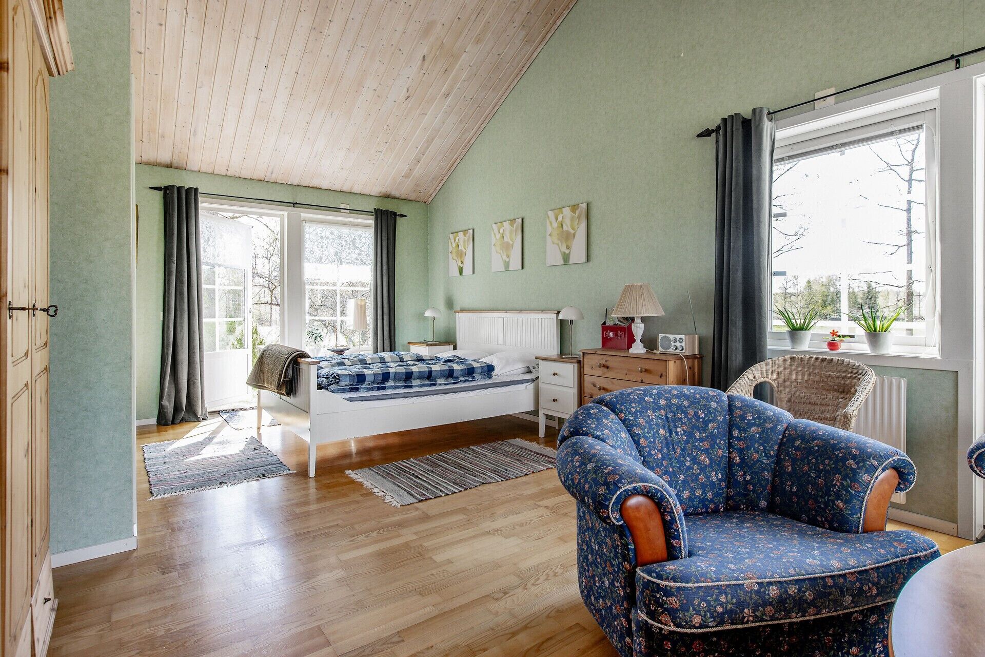Une chambre à coucher comprenant un lit, une chaise, une commode, une fenêtre avec des rideaux et un radiateur.