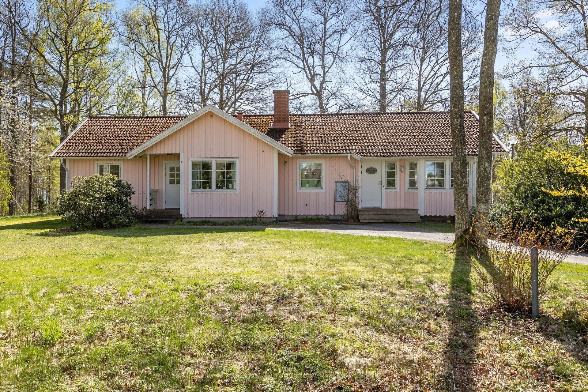 A pink single-story house with a tiled roof, a front porch, and a small front yard.