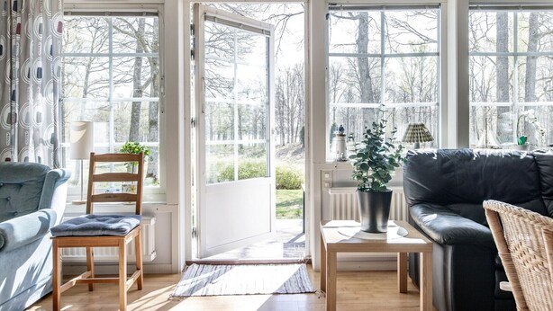 Ein Zimmer mit einer Couch, einem Sessel, einem Tisch und Blick durch große Fenster.