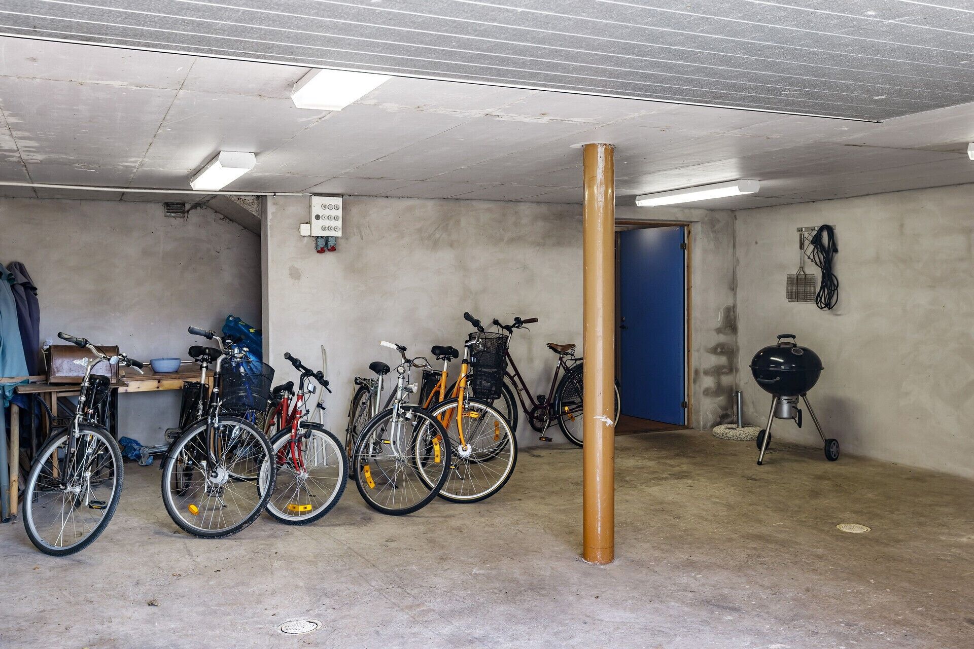 A garage with bicycles, a barbecue grill, and a blue door.