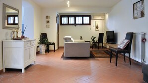 Un salon avec un canapé, un téléviseur et une cheminée. On y trouve une table à manger avec des chaises, ainsi qu’un meuble avec un miroir.