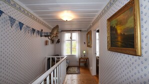 A hallway with patterned wallpaper, a wooden floor, a staircase with a railing, a window with curtains, and a framed painting on the wall. - StayNordic | Idyllic holiday house in Sundshult | SE09011 (Hedekas)