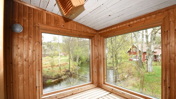 A cabin with wooden walls and large windows overlooking a river and forest. - StayNordic | Idyllic holiday house in Sundshult | SE09011 (Hedekas)