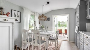 A dining area with a white table and chairs, a hanging light fixture, and a view of the outdoors. - Fantastic cottage with panoramic views of Lake Vidöstern | SE06031 (Vittaryd)