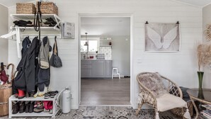 A room with a white wall, a wicker chair, a small table, and a shelf with bags and shoes. - Fantastic cottage with panoramic views of Lake Vidöstern | SE06031 (Vittaryd)