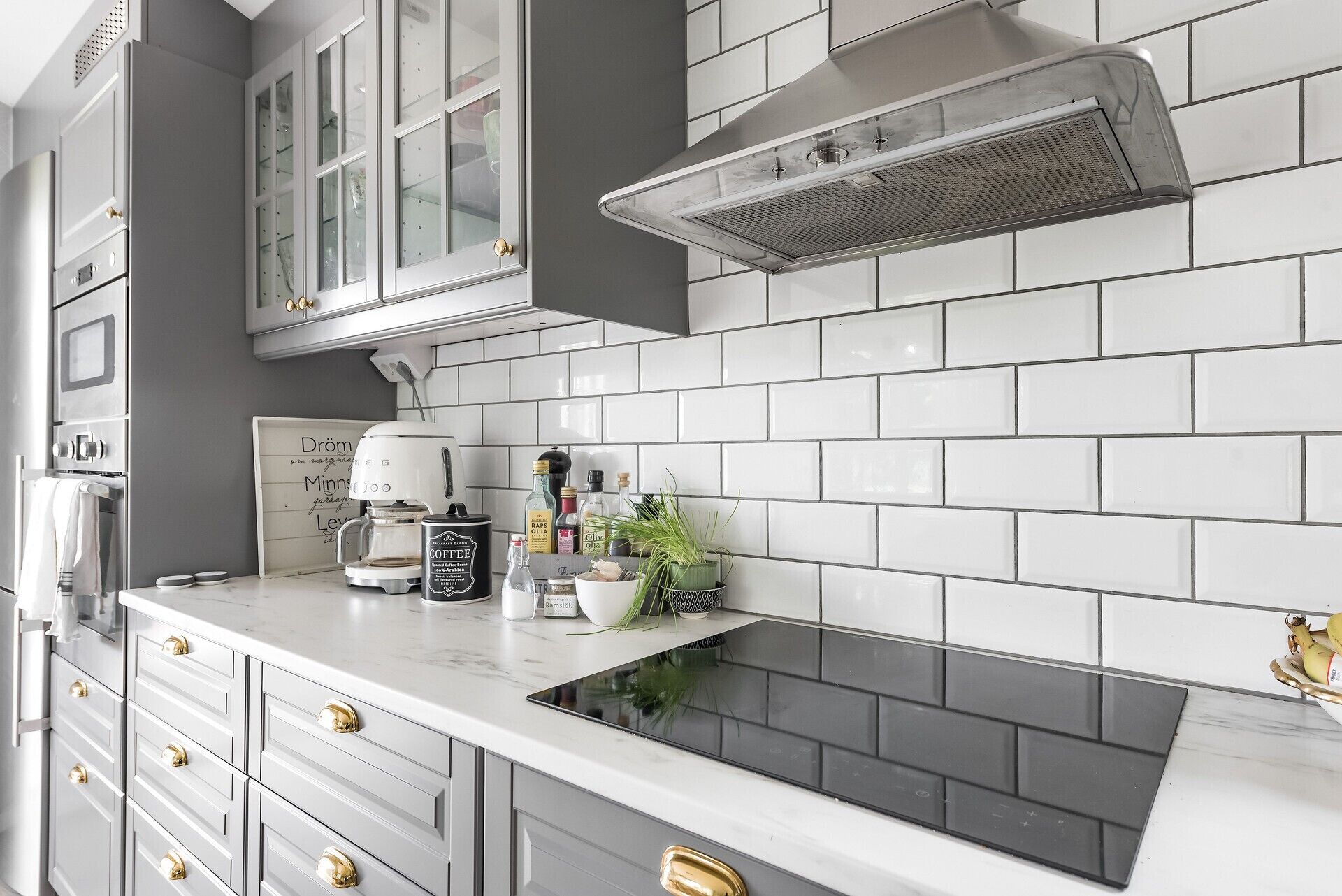 Una cocina con azulejos blancos tipo metro, una cafetera y una estufa.