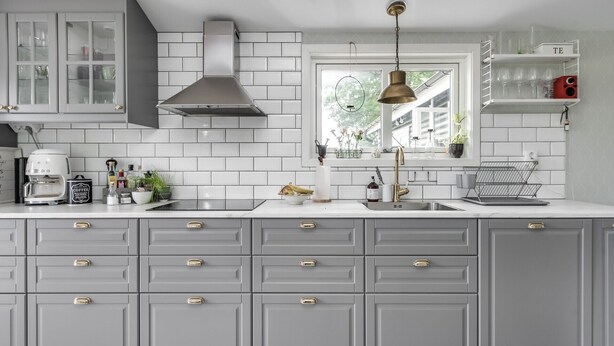 A kitchen with grey cabinets, a stainless steel range hood, a coffee maker, and a window with a view of trees. - Fantastic cottage with panoramic views of Lake Vidöstern | SE06031 (Vittaryd)