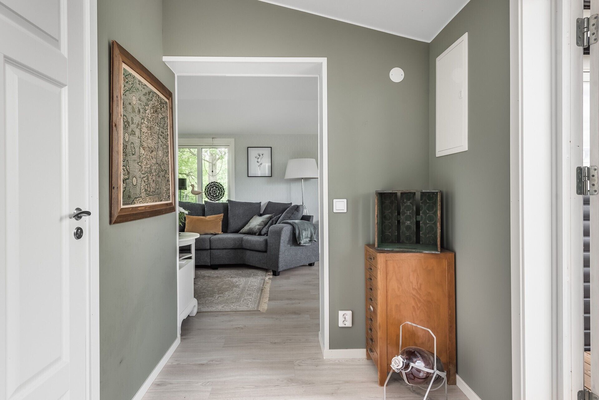 A hallway leading to a living room with a grey sofa, a wooden cabinet, and a framed picture on the wall.