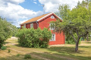 Une maison en bois rouge, avec un toit en pente, entourée de verdure et sous un ciel dégagé.