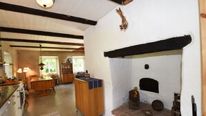 A rustic kitchen with a wooden table and chairs, a built-in oven, and a brick fireplace. - Cozy and modern wing in Boge on Gotland's east coast | SE12011 (Slite)