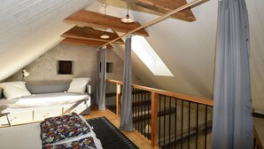 A loft bedroom with a sloped ceiling, wooden beams, a bed, a bench, and a skylight. - Cozy and modern wing in Boge on Gotland's east coast | SE12011 (Slite)